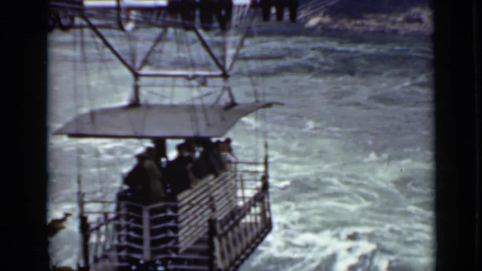 Open gondola with several passengers hangs from cables over a fast-moving Ontario river in 1940 home-movie footage.