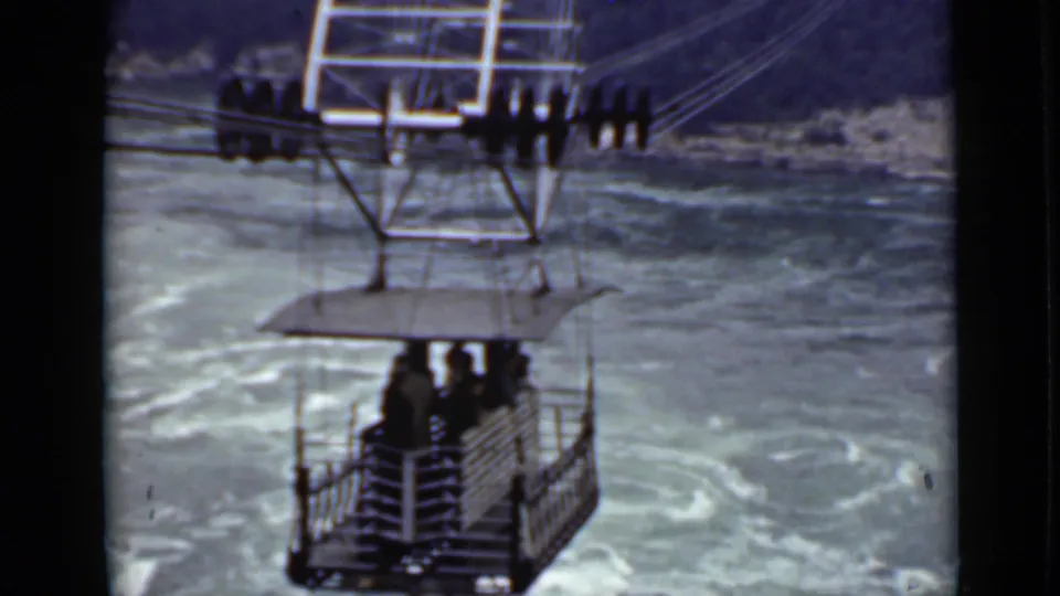 1940 Ontario travel footage frame showing a small open cable car with passengers above swirling river water.