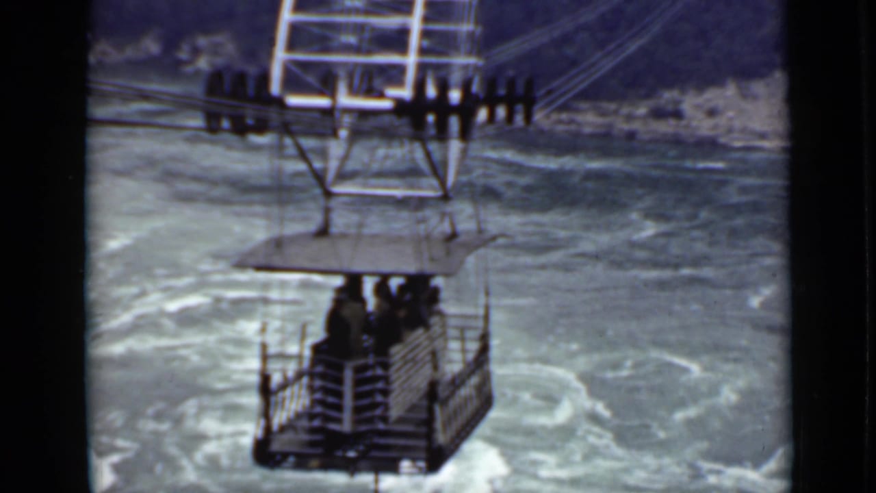 1940 Ontario home-movie frame showing an open cable car with passengers suspended over turbulent water.