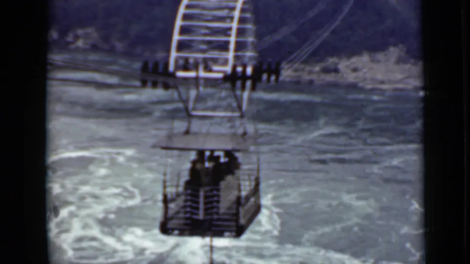 1940 Ontario 8mm frame with passengers in an open cable car above foamy, swirling water.