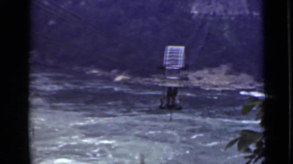 Wide 1940 Ontario home-movie view of a cable car crossing above a fast river between wooded banks.