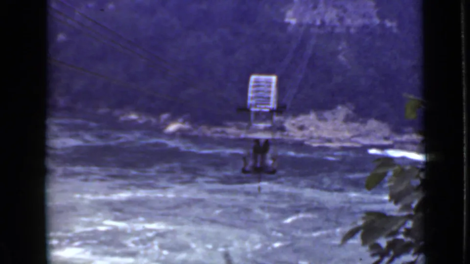 1940 Ontario 8mm footage frame with a small suspended cable car above rapids and foreground leaves at the edge.