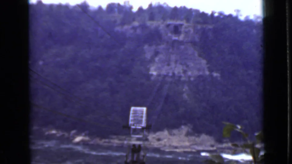 1940 Ontario home-movie frame showing a broad river below wooded hills, with a utility pole and wires crossing the foreground.