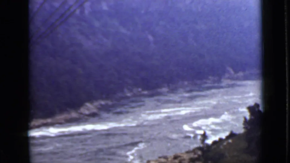 1940 Ontario river view with pale rapids, rocky shoreline, and dense trees along the far bank.
