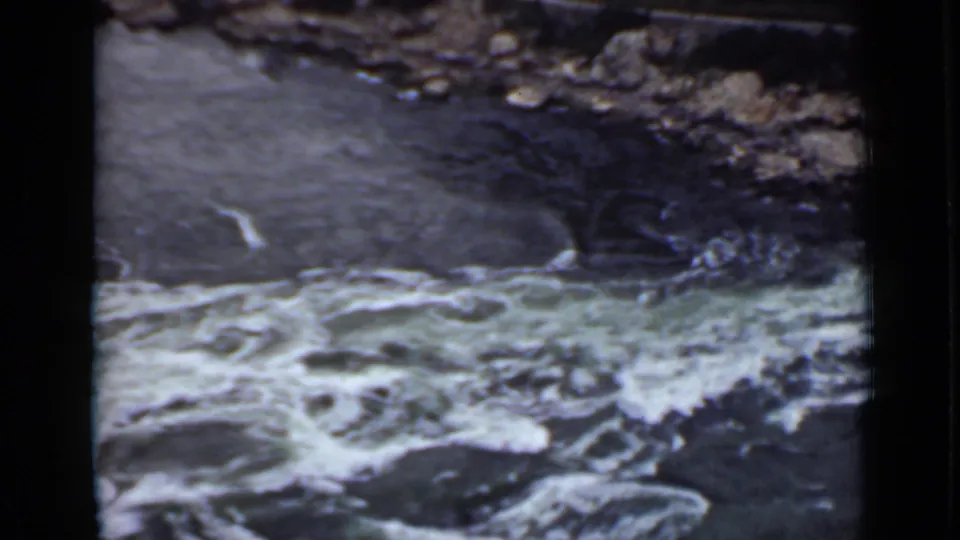 1940 Ontario 8mm frame showing whitewater filling the foreground with stones and a rough bank beyond.