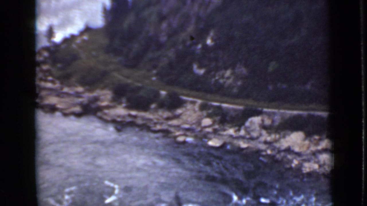 Rocky river gorge with water, cliffs, trees, and a narrow road along the slope.