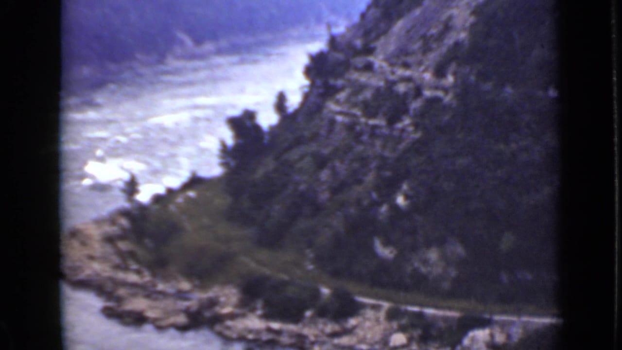 Elevated view of a river bend, rocky cliff, trees, and a road near the water.