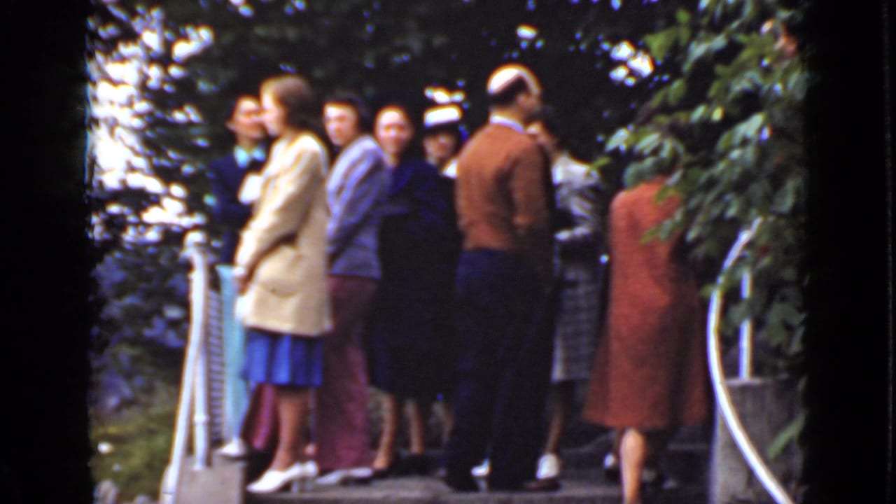 Adults stand close together on a deck beside railings and dense greenery.