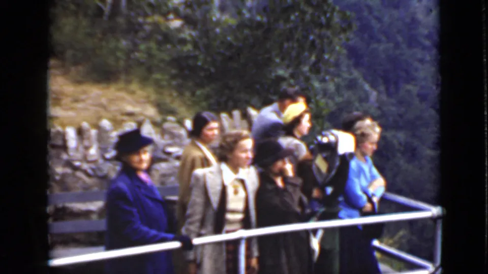 Adults in period outerwear stand by a railing at an Ontario scenic overlook, with a stone wall and trees behind them.