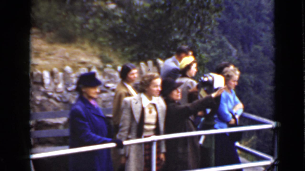 Adults in coats and hats stand beside a metal railing at a scenic overlook.
