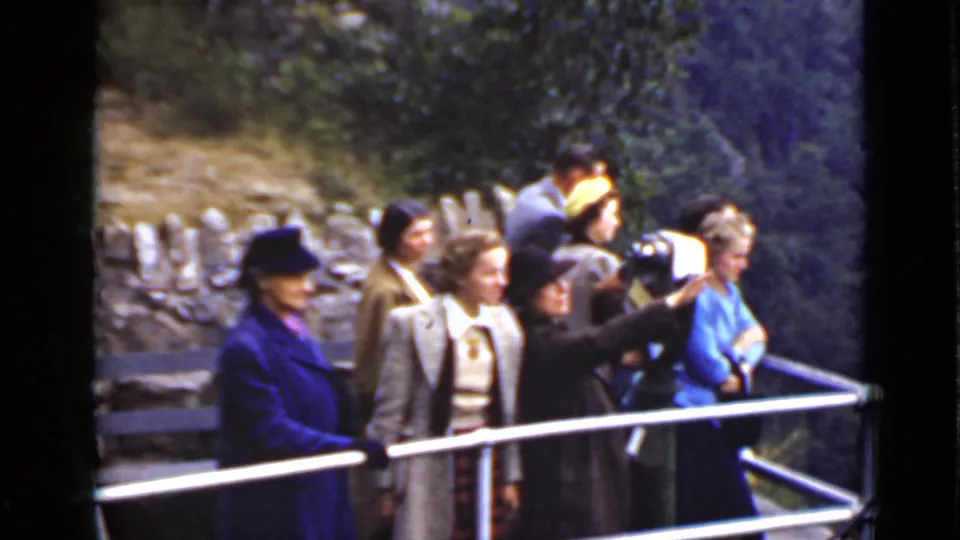 In Ontario, Canada, adults in period coats and hats stand on a railed deck and look toward the surrounding landscape.