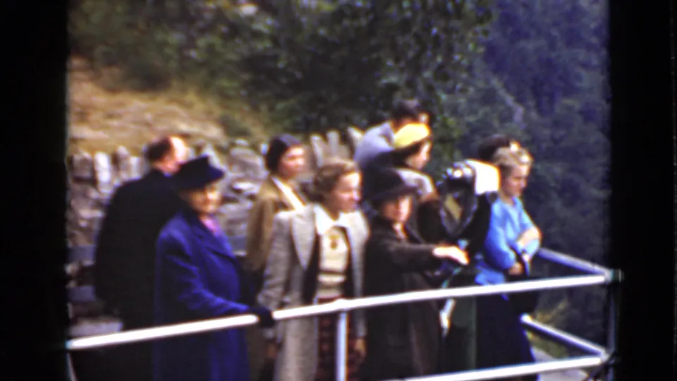 A group of adults in 1940s-style dress stands at an Ontario overlook railing, including a woman in a vivid blue coat.
