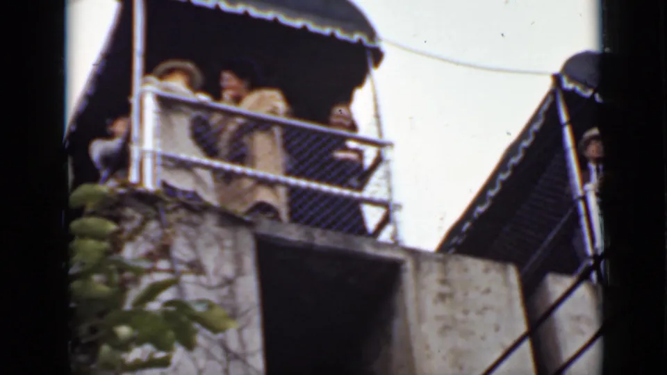 Adults appear on an elevated viewing balcony in Ontario, seen from below beside a light-colored building and railing.