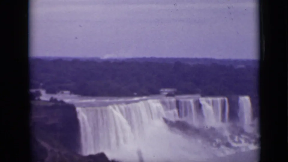1940 Ontario home-movie frame showing a soft, faded view of Niagara Falls with white water, spray, and a dark distant shoreline.