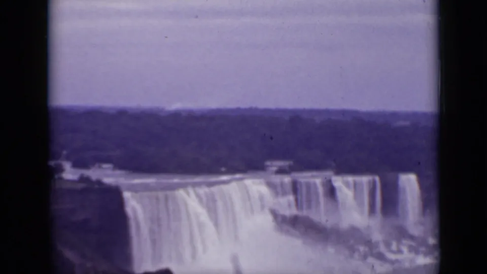 1940 Ontario 8mm frame showing Niagara Falls across the river, with broad curtains of water, mist, shoreline, and visible film gate edges.