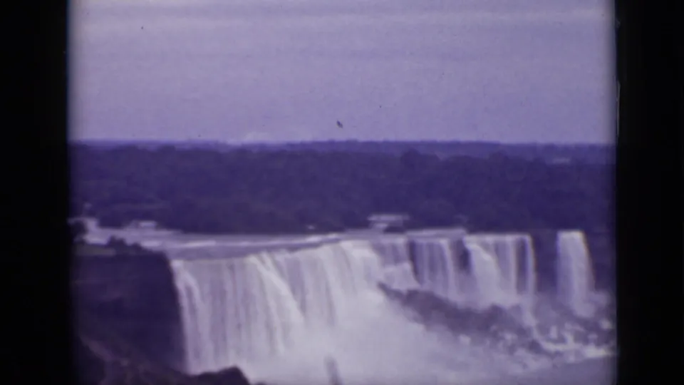 High-angle 1940 8mm view of Niagara Falls in Ontario, with broad water curtains, spray, dark landforms, and a purple film cast.