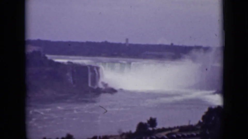 Soft 8mm frame of Niagara Falls in Ontario, with mist rising from the cascade and a distant tower-like structure beyond the river.