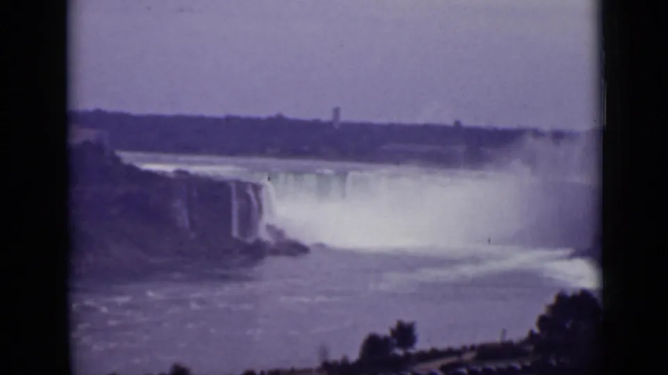 1940 home-movie frame of Niagara Falls, with broad spray, rushing river water, dark frame borders, and faint shoreline details.