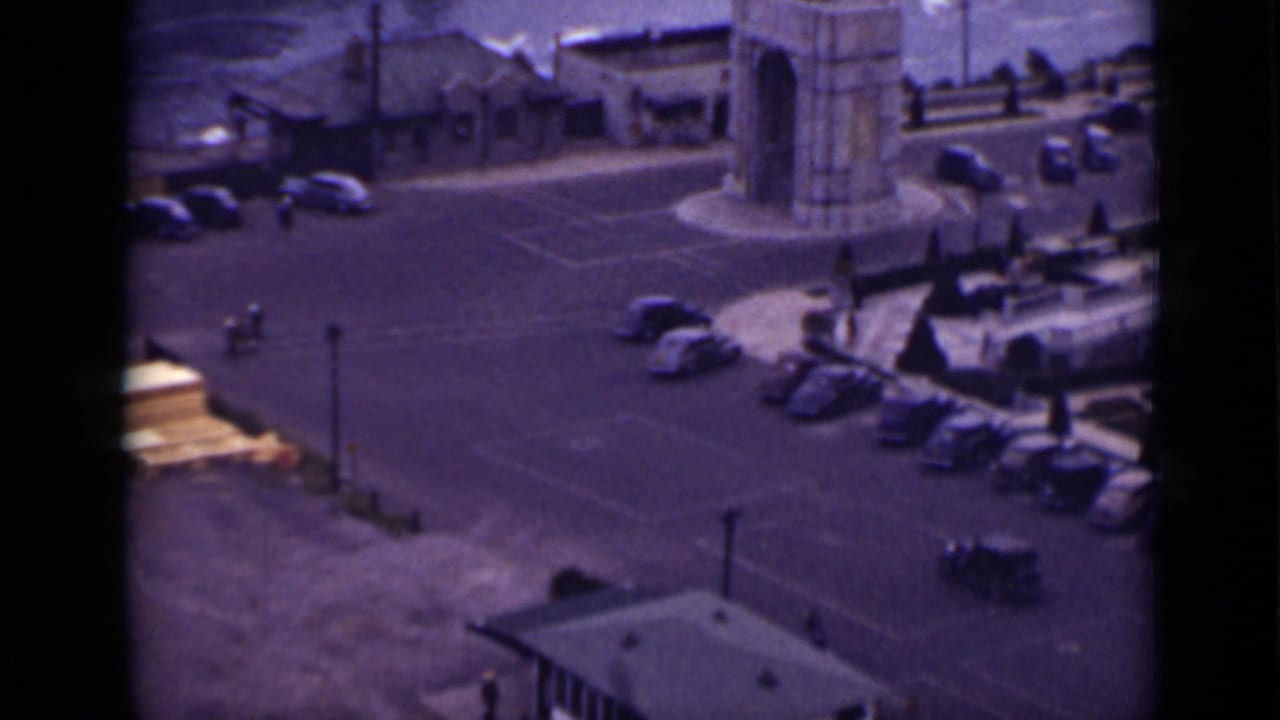 Paved parking lot near water with rounded cars, a stone arch, railings, and small pedestrians.
