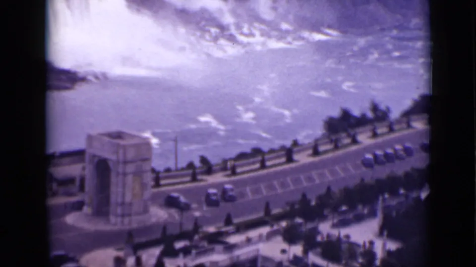 1940 Ontario Niagara Falls home-movie frame emphasizing misty water beyond the overlook, with the arch and parked cars below.