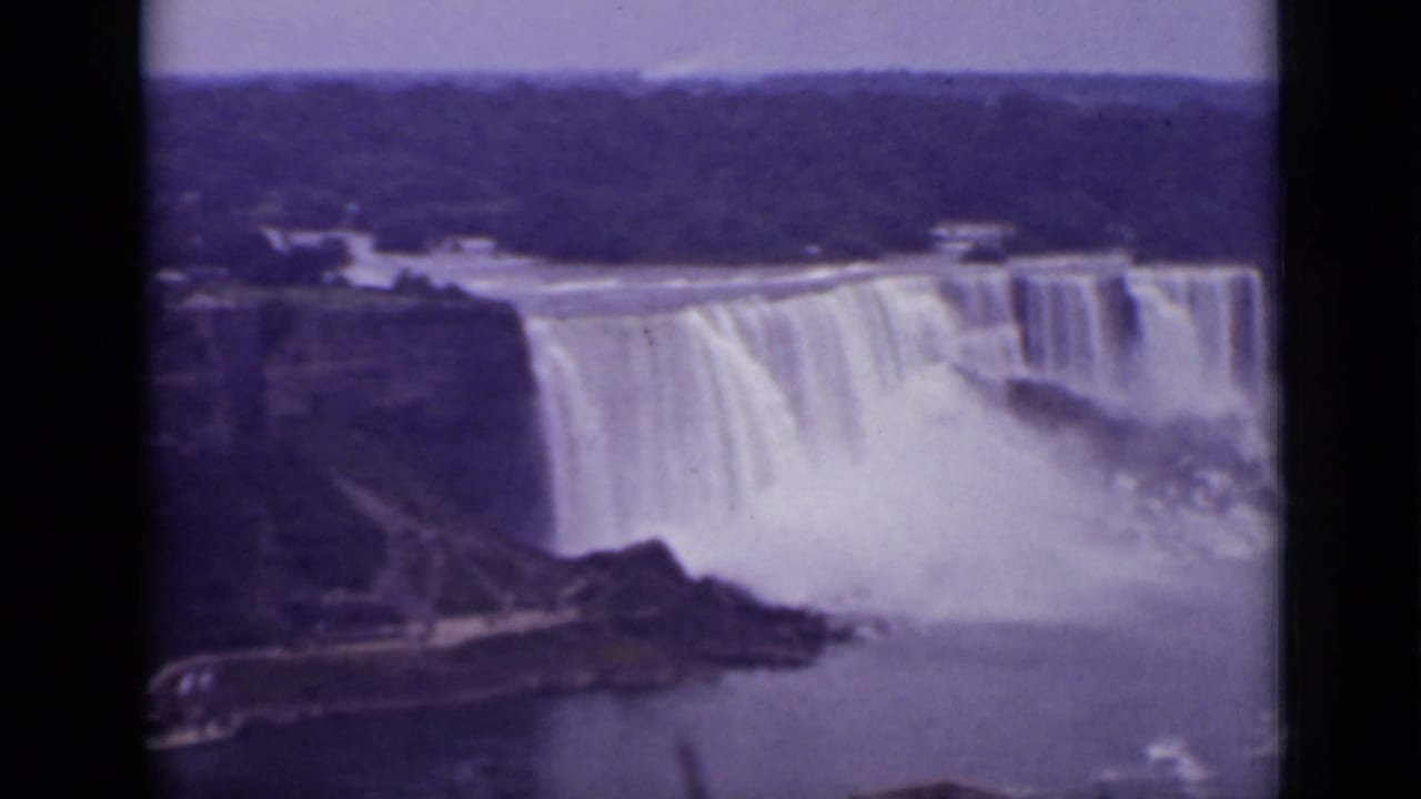 Wide aerial view of Niagara Falls with mist and wooded shoreline.