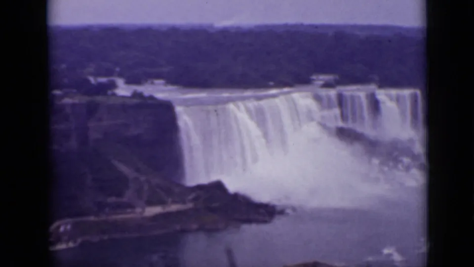 1940 8mm view over Niagara Falls, Ontario, showing cascading water, mist, rocky edges, and distant trees.