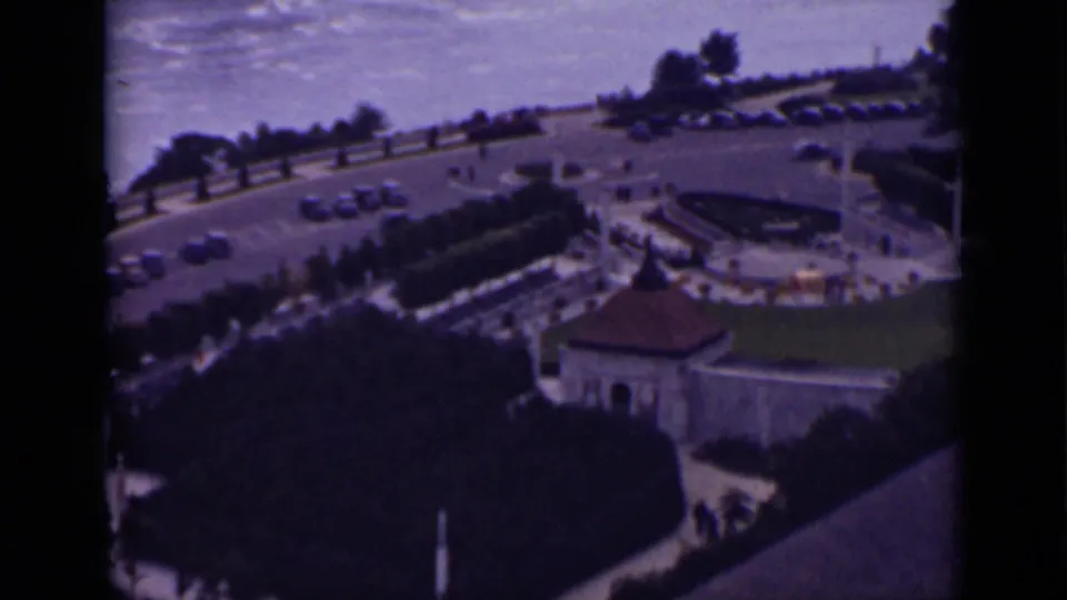 1940 8mm overhead view near Niagara Falls, Ontario, with parked cars, visitors on paths, lawns, trees, and roofed structures.