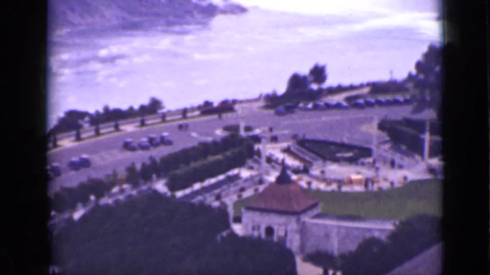 1940s Ontario home-movie view over Niagara Falls with a curved road, parked cars, landscaped grounds, and a small stone building.
