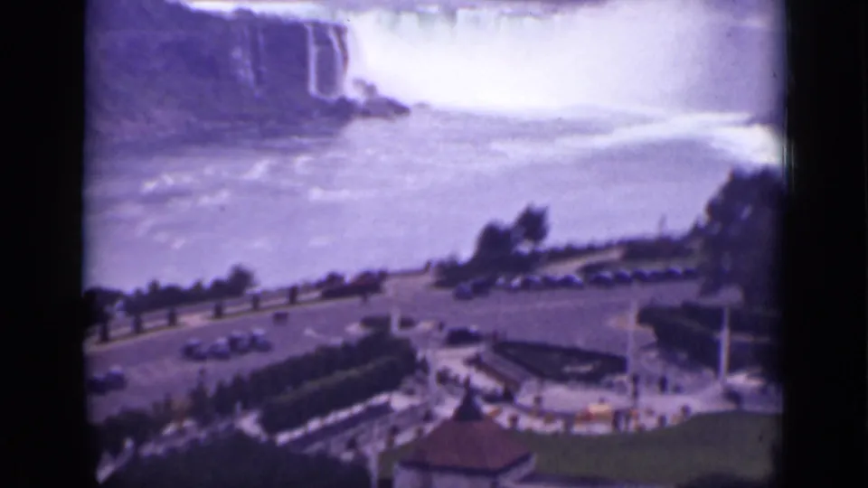 Niagara Falls appears beyond a visitor road and parking area, with mist rising over the river in faded 8mm color.