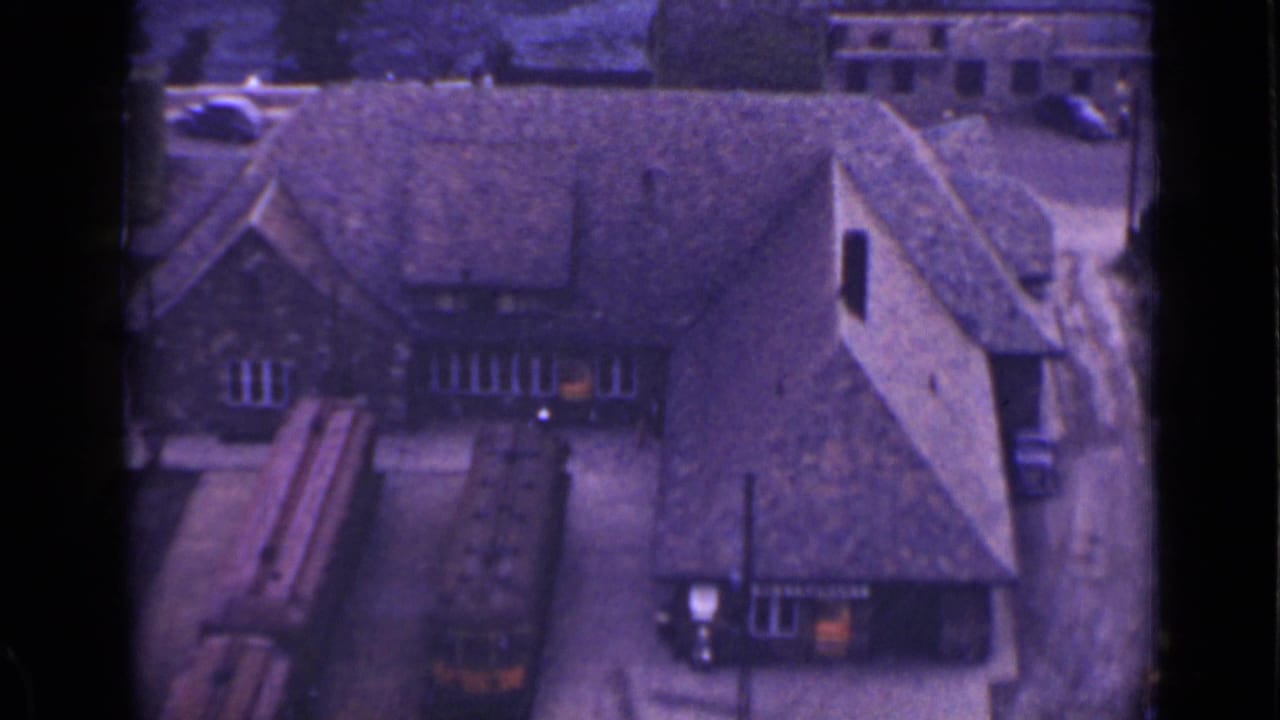 Elevated view of a steep-roofed building with nearby vehicles and a yard.