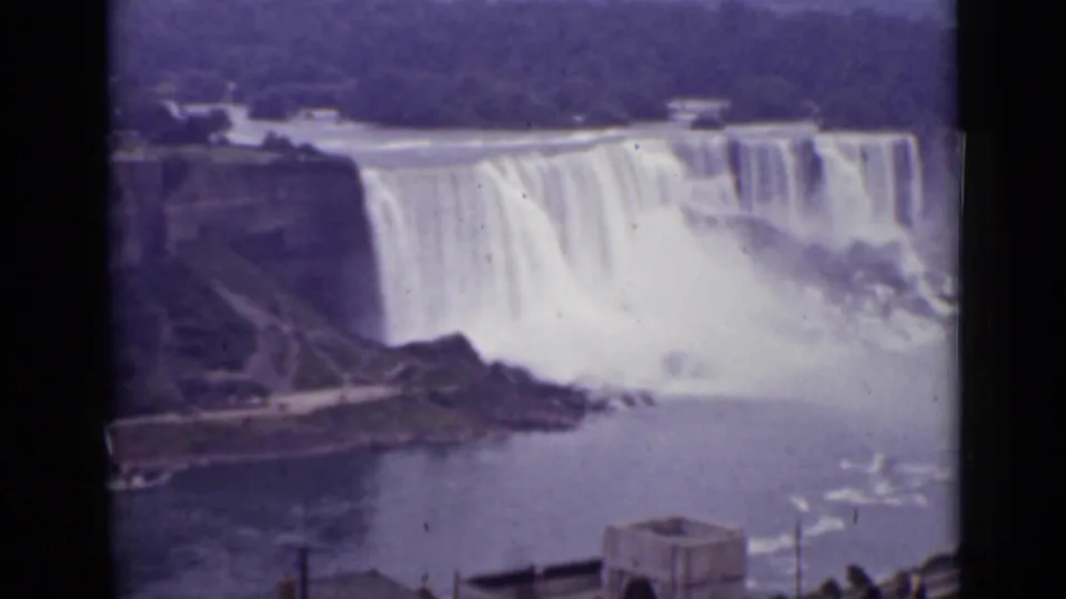 Distant 1940 Ontario view of Niagara Falls cascading over the cliff edge with mist rising from the base.