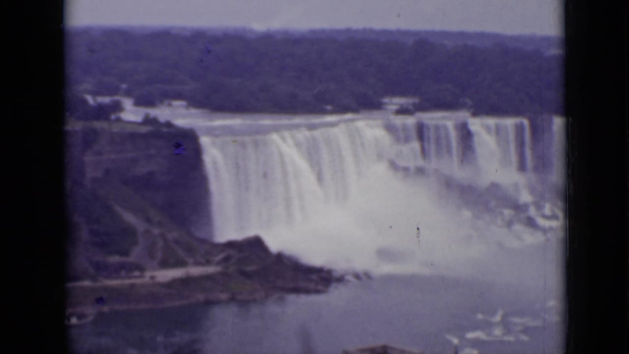 Wide view of Niagara Falls with water dropping over cliffs and mist rising below.