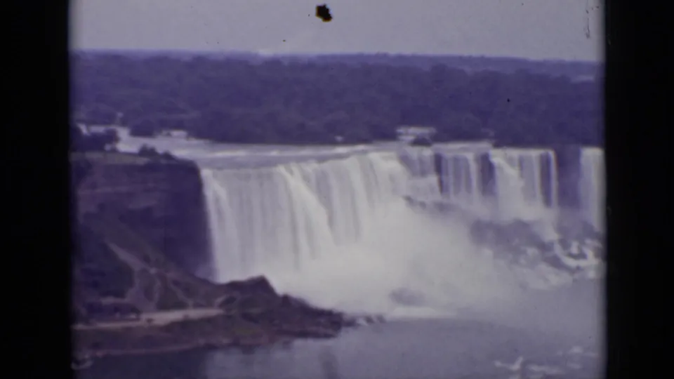 Static 1940 Ontario home-movie frame showing Niagara Falls, surrounding cliffs, white spray, and a distant wooded horizon.