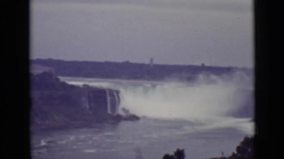 1940 8mm frame of Niagara Falls from a lower river angle, with spray obscuring part of the falls and shoreline in the foreground.