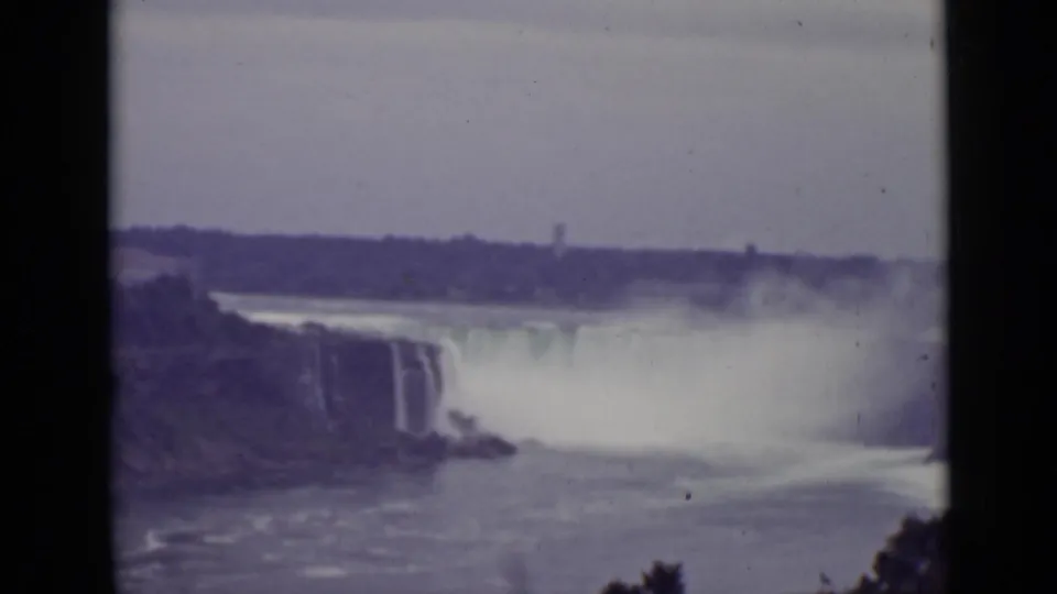 Vintage 1940 Ontario view across the river toward Niagara Falls, where spray covers much of the falls beneath an overcast sky.