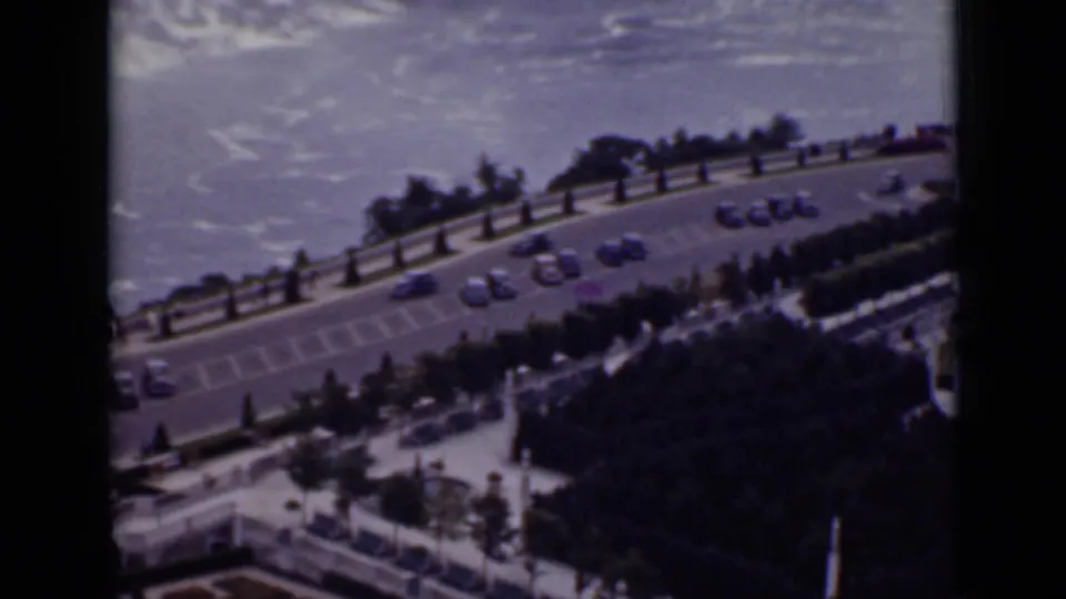 1940 Ontario 8mm frame looking down toward a riverside road near Niagara Falls, with cars, railings, trees, and water beyond.