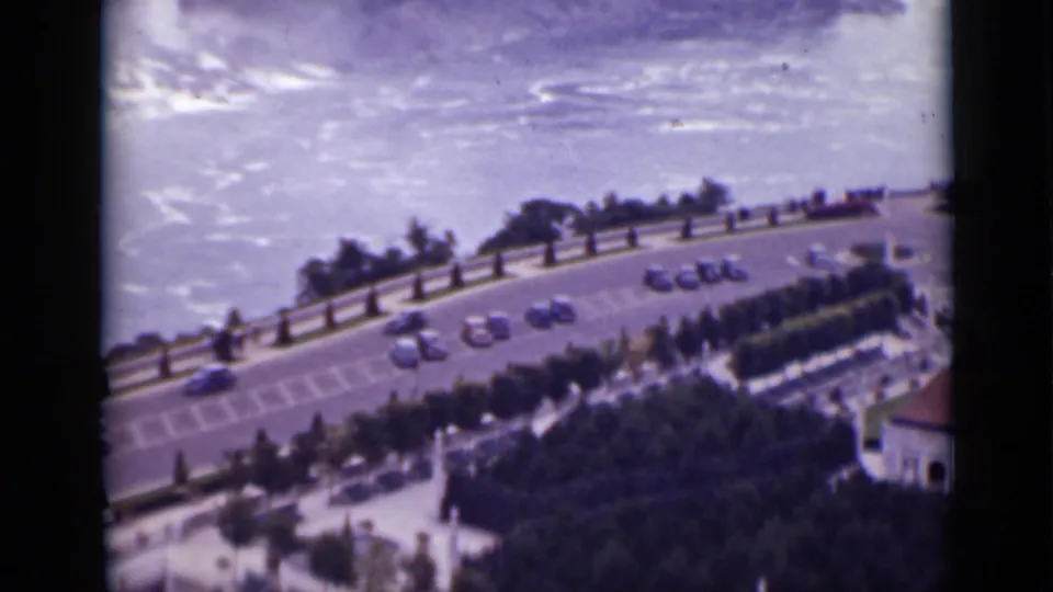 Elevated 1940 Ontario home-movie view of cars along a riverside road near Niagara Falls, with trees, railings, and pale water in the background.