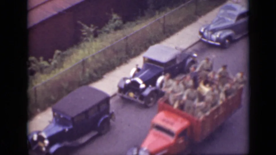 1940 home-movie frame showing period cars and a red open truck carrying visible passengers on a road in Ontario.