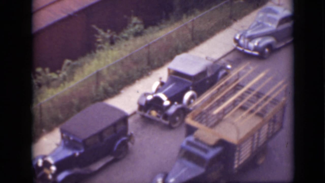 Vintage cars and an open passenger truck seen from above on a street near a sidewalk.