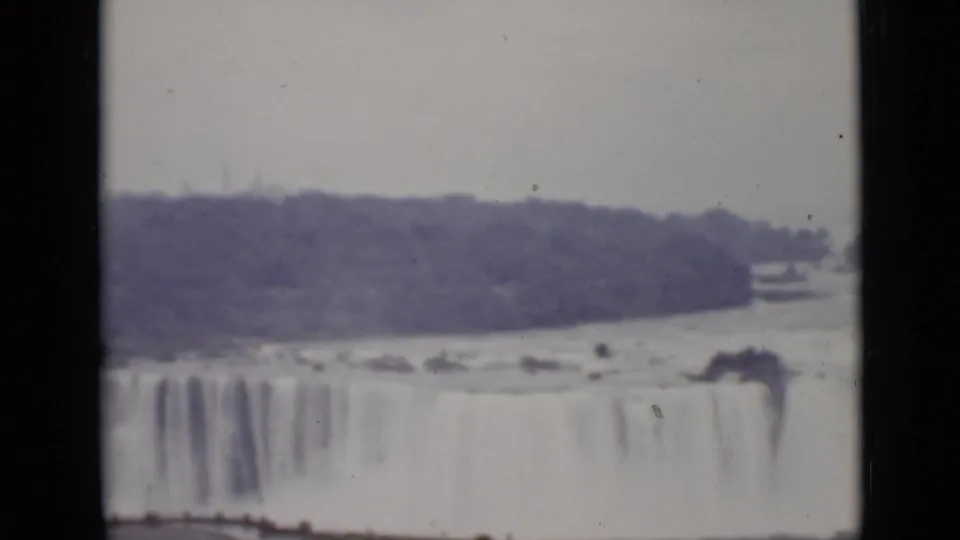 1940 Ontario home-movie view of Niagara Falls from a distance, with water dropping across the frame and wooded banks beyond.