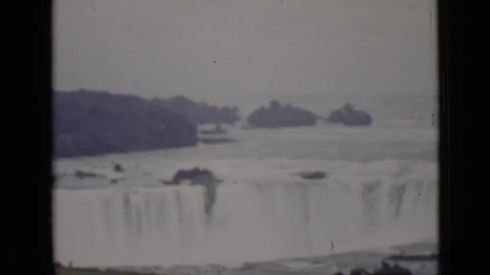 Ontario-side 8mm frame of Horseshoe Falls with the broad cascade edge, hazy mist, dark island shapes, and visible film gate borders.