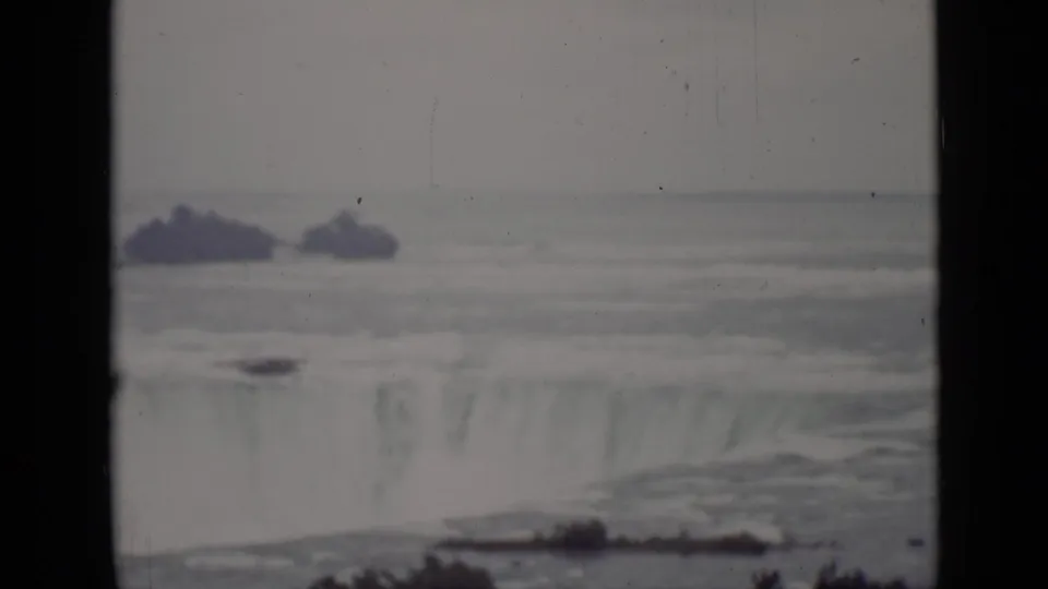 1940 Ontario 8mm view of Niagara Falls from a distance, with water flowing over the rim and dark film-frame borders visible.