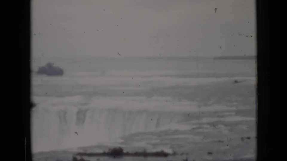 Distant 1940 Ontario view of Niagara Falls, showing the waterfall edge, pale river water, mist, and dark vertical 8mm borders.