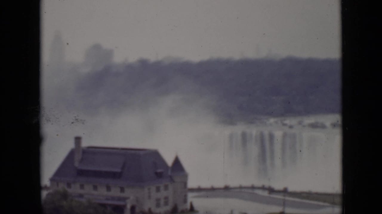 American Falls with mist behind a stone riverside building, seen through dark vertical framing.