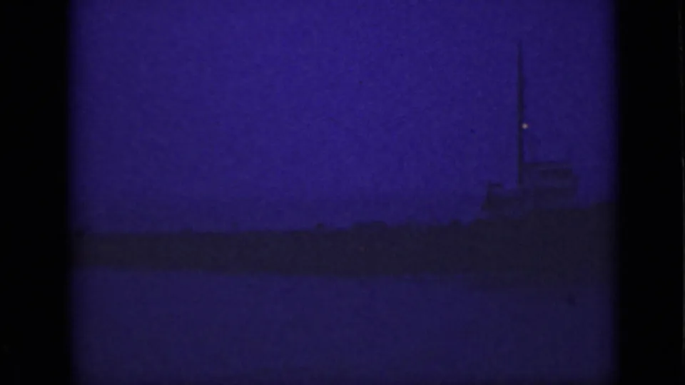 Underexposed purple 8mm frame from the Niagara River area, with a faint shoreline and silhouetted structure on the horizon.