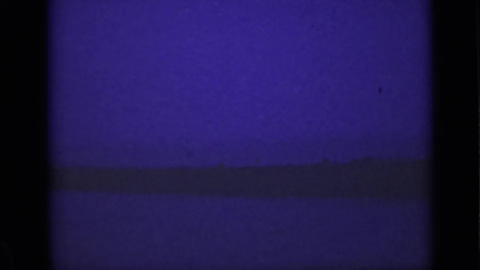 Purple-tinted, underexposed 8mm frame showing mostly river and a low dark shoreline near Niagara Falls.