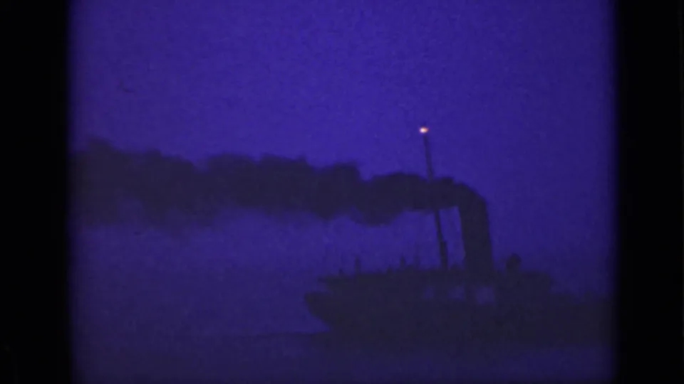 1940 Ontario 8mm frame of a vessel on dark water, with smoke trailing and a small light glowing above the silhouette.