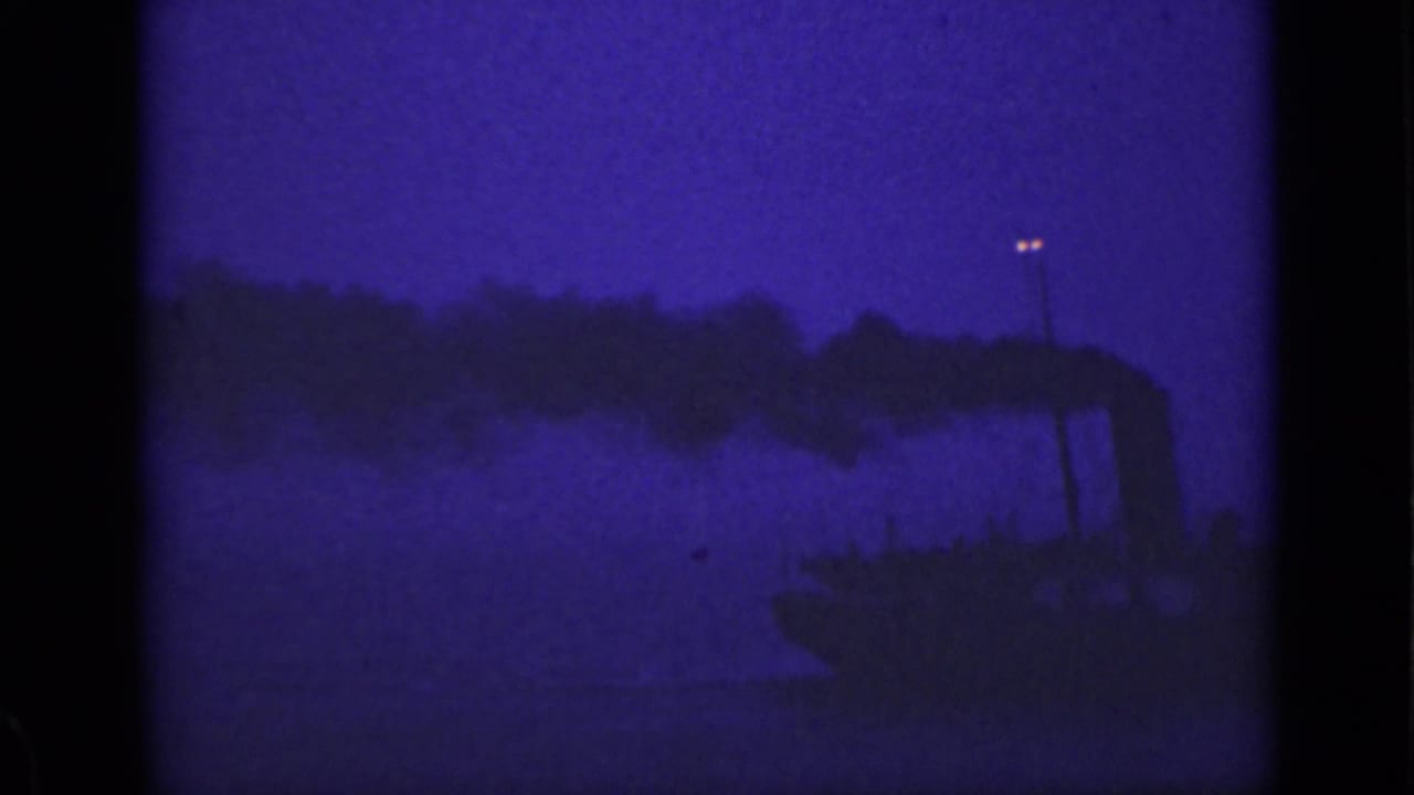 Dark boat stack silhouette releases smoke against a blue-purple night sky over water.