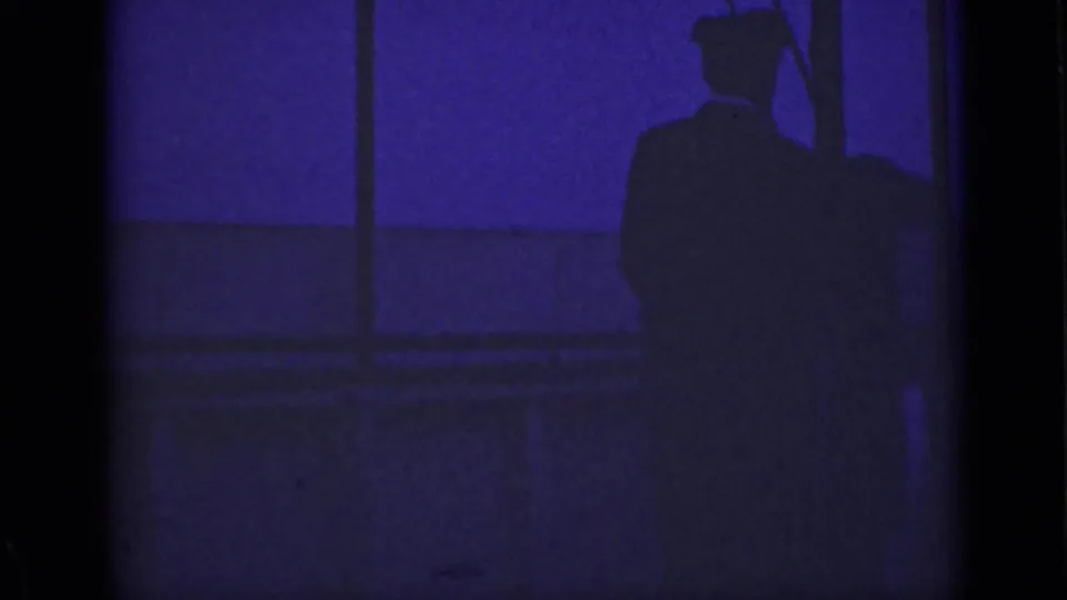 A silhouetted adult on an Ontario boat deck appears beside posts and railings in this 1940 low-light home-movie frame.