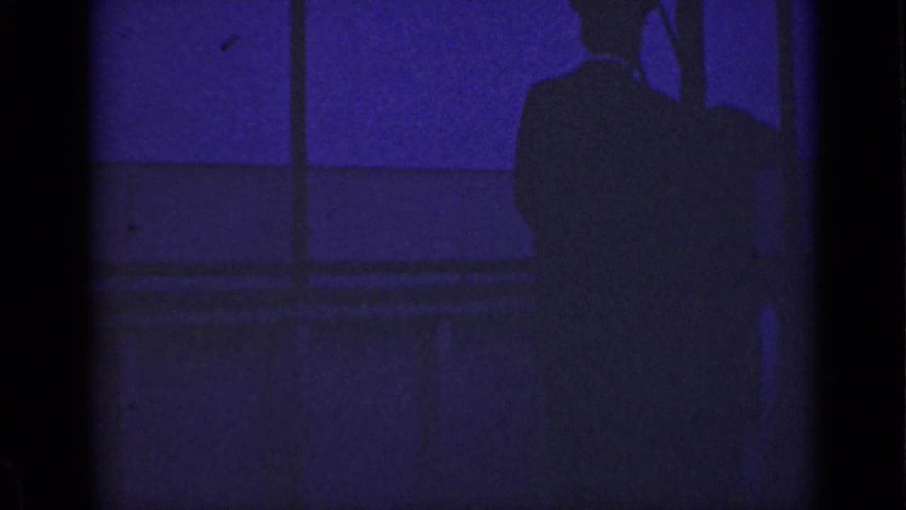 Dark silhouette of a man standing near railing lines in a blue-purple waterfront scene.